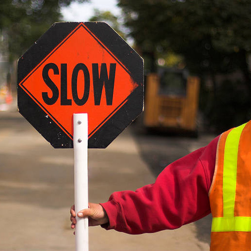 Flagger directing traffic, holding "Slow" sign
